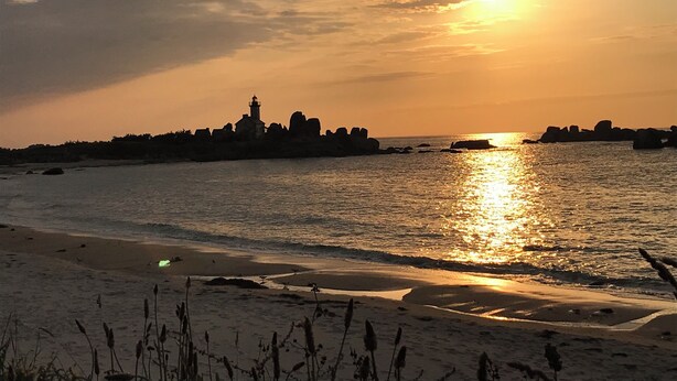 A coastal sunset with a lighthouse silhouette, calm sea, and sandy beach.
