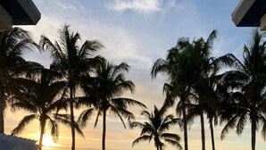 A poolside area with lounge chairs and umbrellas, palm trees, and a sunset view. - GULF VIEWS, PRIVATE BEACH CLUB, AVAIL NOV-DEC 2027 (Naples)