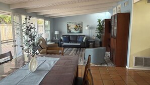Un salon comprenant une table à manger, des chaises, un canapé, une table basse, une lampe, un tableau et un ventilateur de plafond.