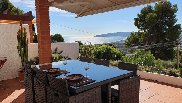 A patio with a table set for two, overlooking a scenic view of the sea and hills.