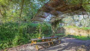 A picnic table under a thatched roof in a wooded area. - Superior-Category Country Houses in a Natural Park. Nature and comfort. (Galaroza)