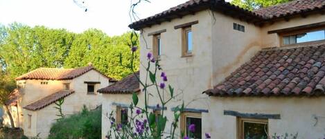 A row of traditional buildings with tiled roofs, surrounded by lush greenery and flowering plants.