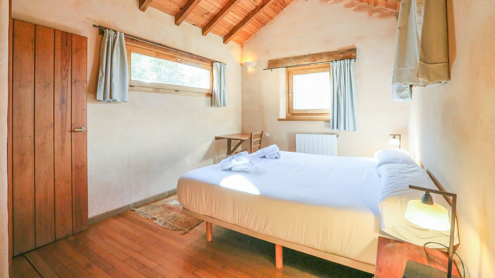 A bedroom with a wooden bed, a nightstand, a window with curtains, a radiator, and a wooden wardrobe.
