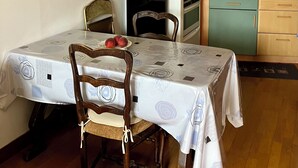 Een eetgedeelte met een tafel voor twee personen, een zwarte koelkast, houten stoelen en een keuken met een betegelde spatwand en houten keukenkastjes.