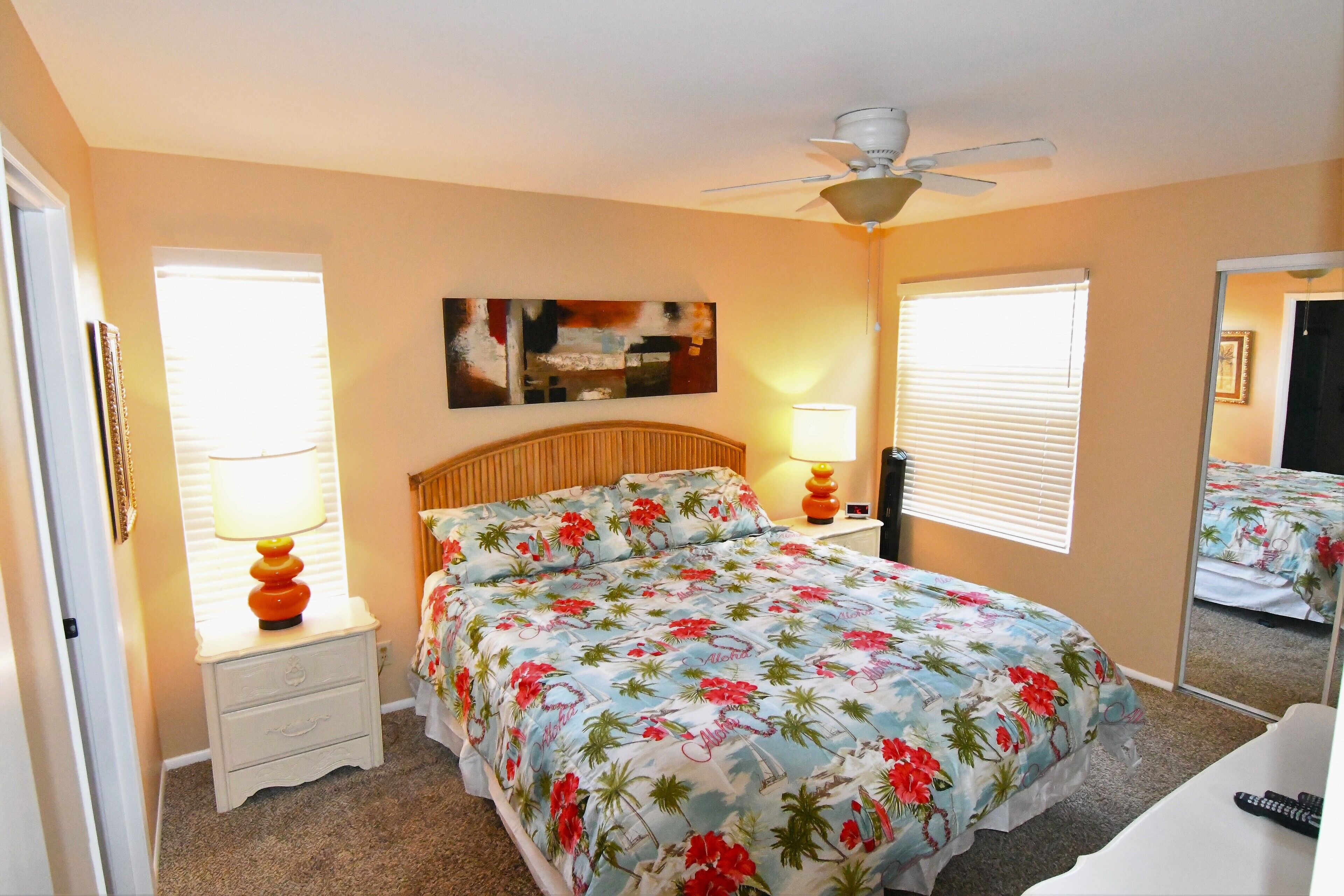 A bedroom with a bed, nightstands, a ceiling fan, and a large mirror.