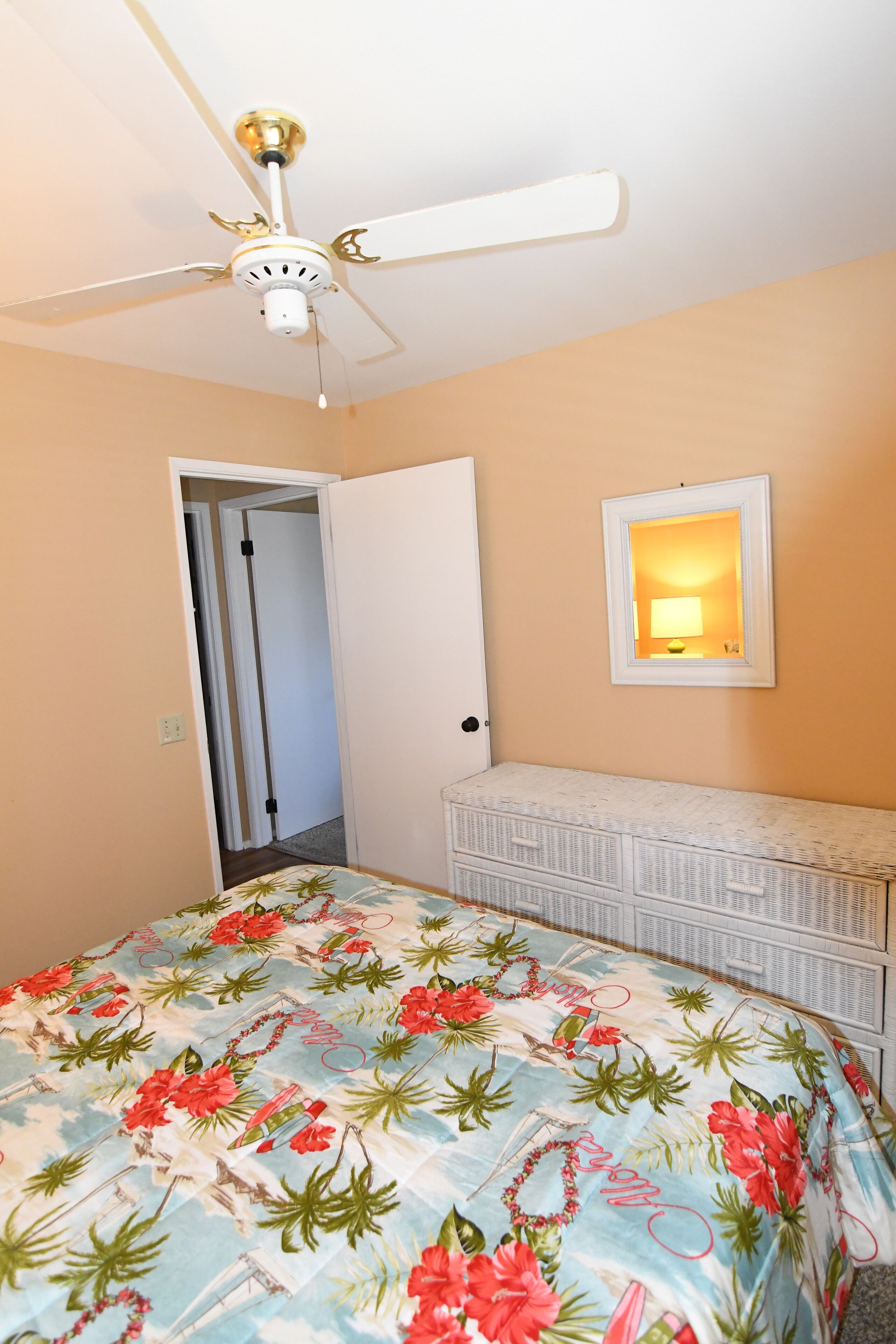 Een slaapkamer met een bed, een plafondventilator, een deur en een dressoir.
