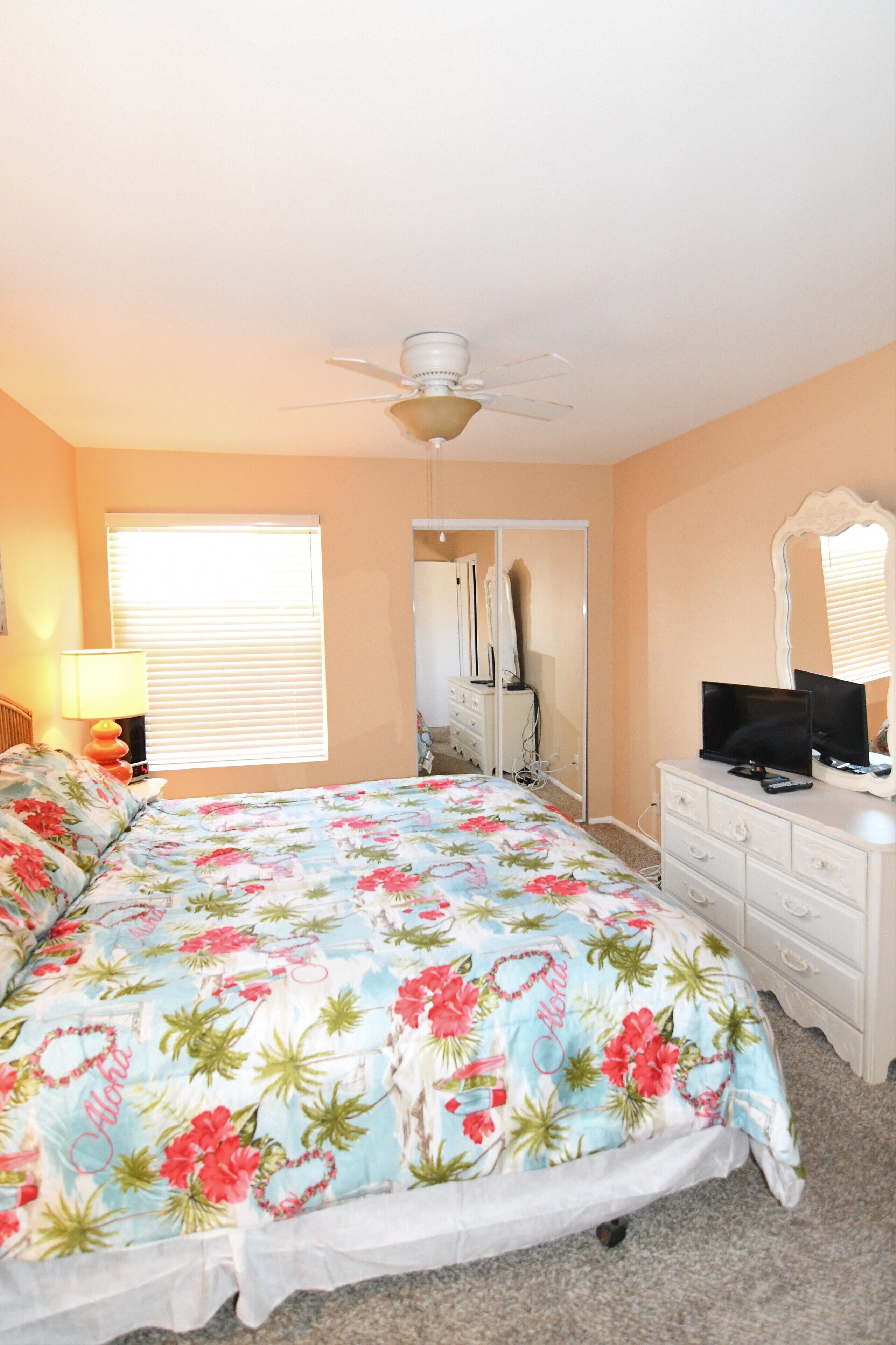 A bedroom with a bed, a dresser, a television, a ceiling fan, and a window with blinds.