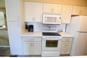 A kitchen with white cabinets, a microwave, an oven, and a refrigerator.