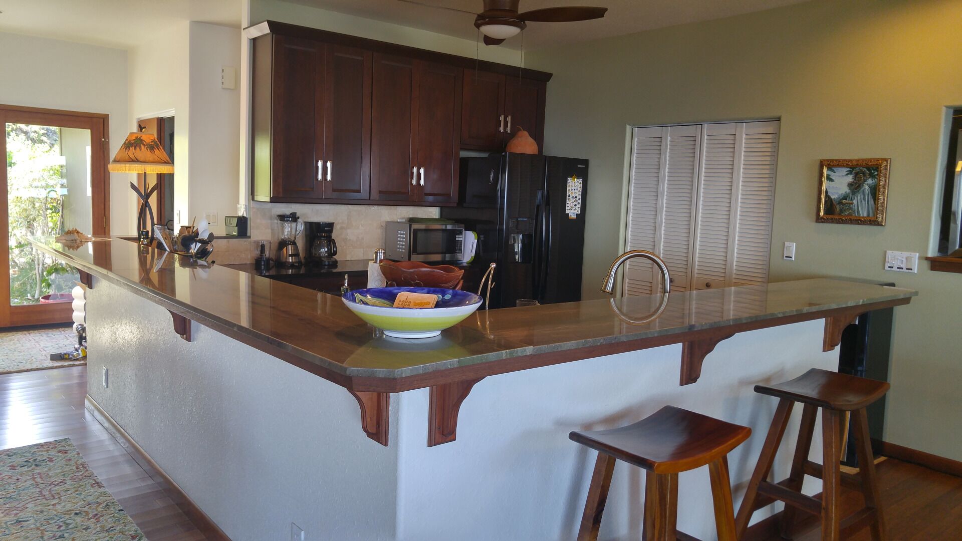 A kitchen with dark wooden cabinets, a large island with stools, a refrigerator, and a microwave.