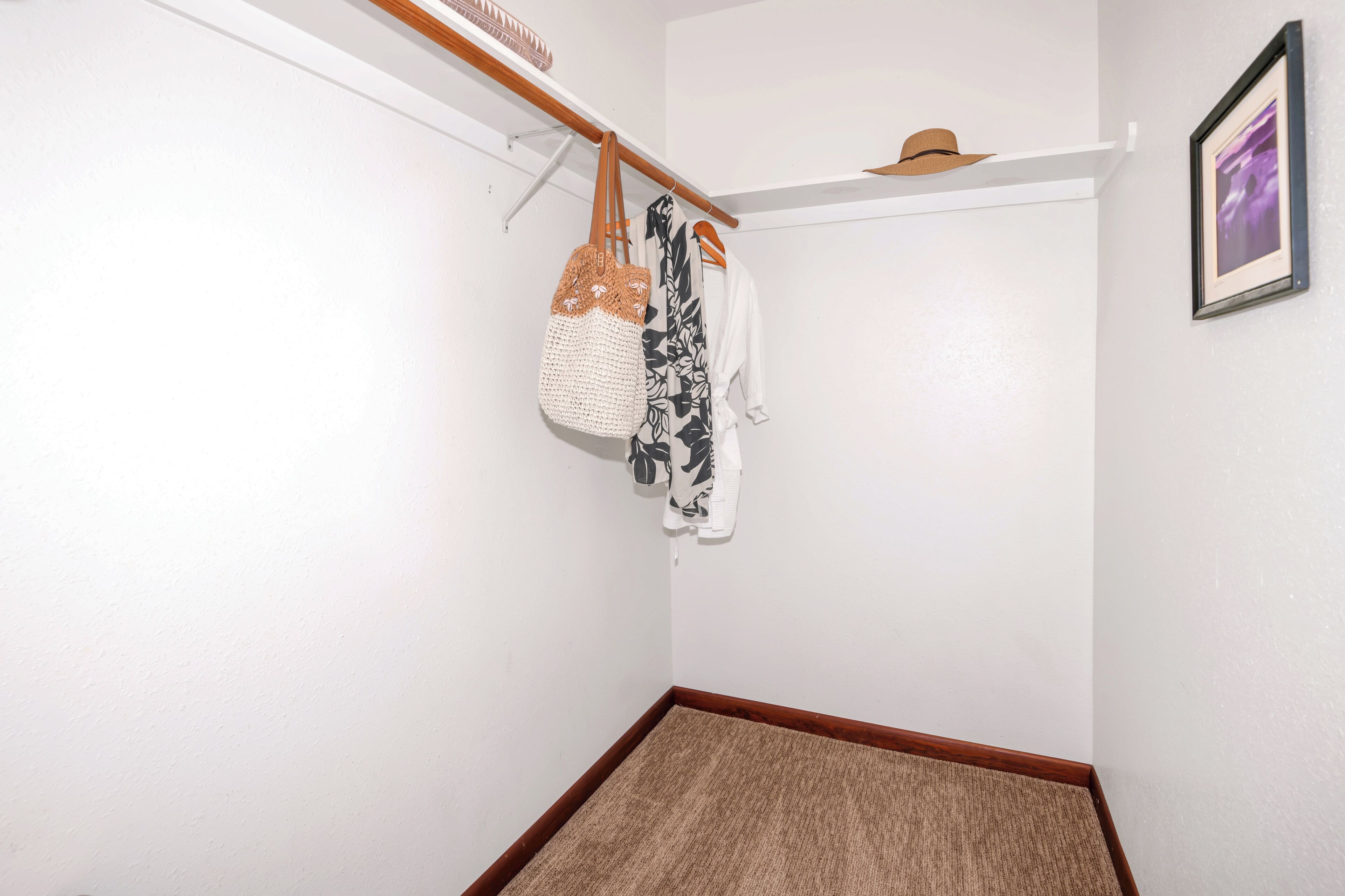 A corner of a room with a wooden floor, a white wall, and a white door. There is a white bag hanging on a wooden rack, and a hat on a shelf above the door.