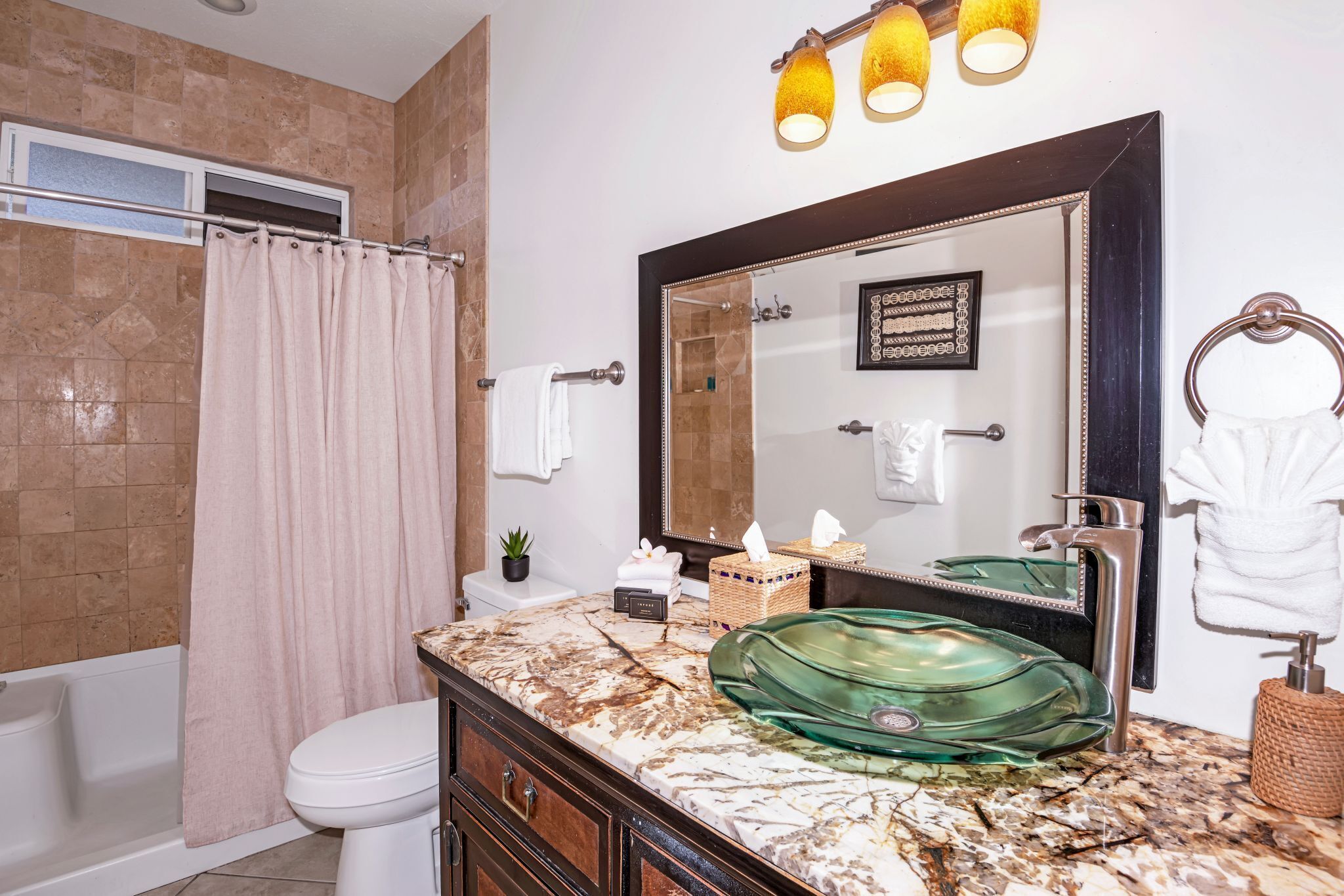 A bathroom with a marble countertop, a green glass sink, a large mirror, and a shower curtain.