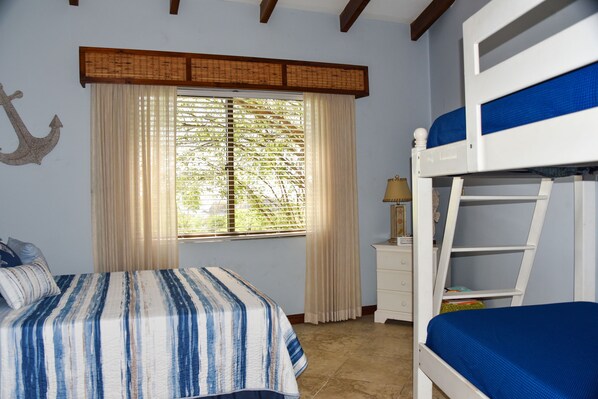 A bedroom with a bunk bed, a bedside table with a lamp, a window with curtains, and a wall-mounted anchor decoration.