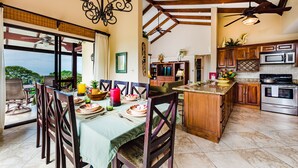 Une cuisine spacieuse avec des poutres en bois, un coin repas avec une table dressée pour quatre personnes, et une vue sur l’extérieur.