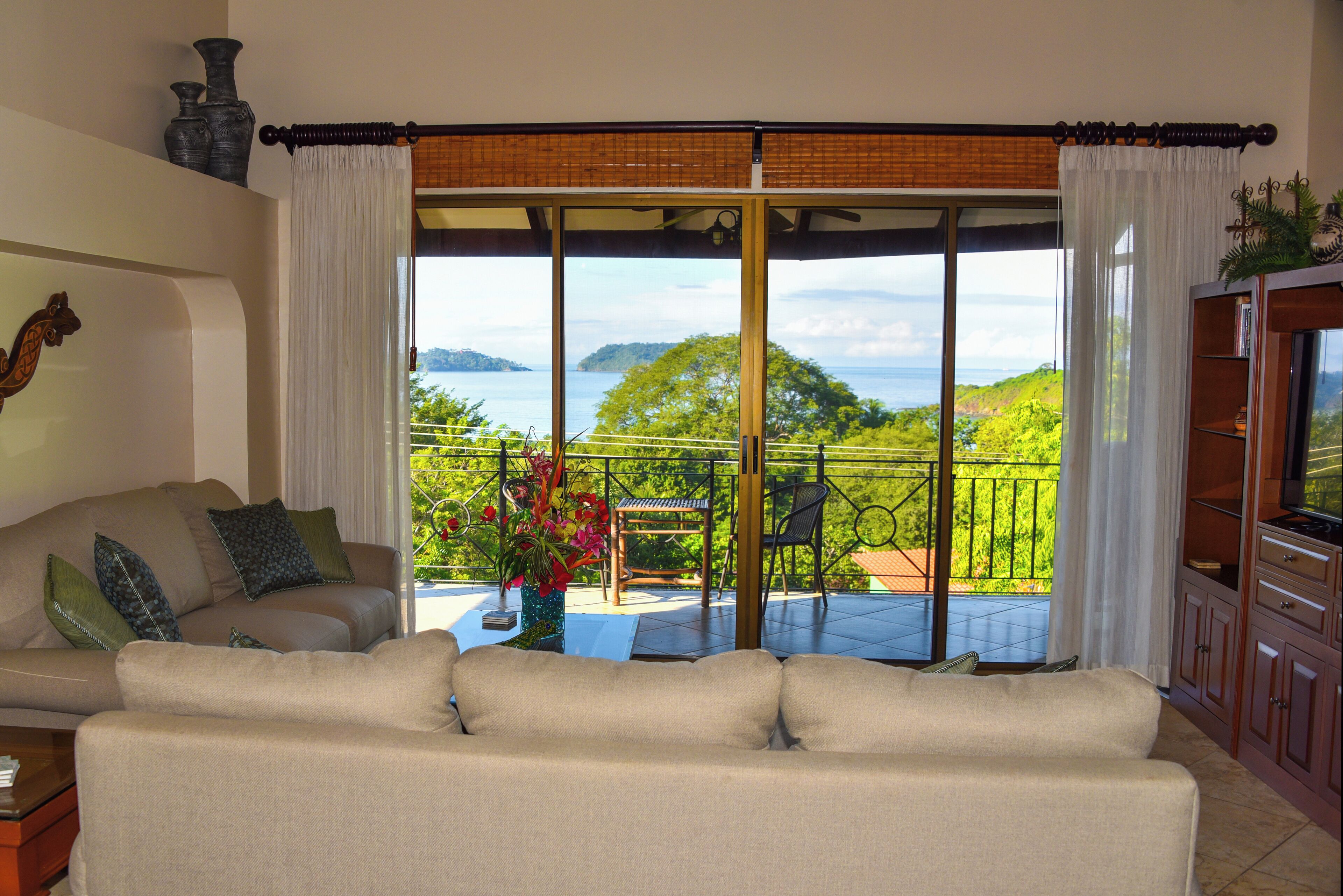 A living room with a sofa, a coffee table, and a view of a balcony with a table and chairs.