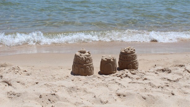 A sandy beach with two sand sculptures and a pink inflatable in the water.