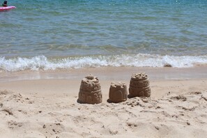 Una playa arenosa con dos esculturas de arena y un flotador rosa en el agua.