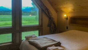 Ein Schlafzimmer mit großem Fenster, einem Bett mit ordentlich gefalteten Handtüchern, einem Deckenventilator und einer Wandleuchte.