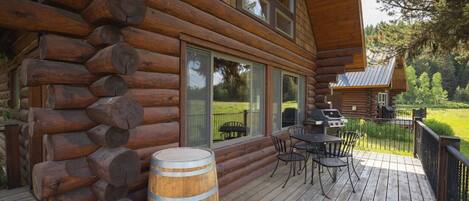 A log cabin with a deck, outdoor seating, and a barbecue grill.
