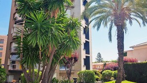 A multi-story building with balconies, surrounded by palm trees and well-maintained grass. - Big Apartment, Sea & Mountain views, private pool, close to amenities & IronMen  (Calella)