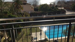 A balcony with a view of a swimming pool, palm trees, and a building with a tiled roof. - Big Apartment, Sea & Mountain views, private pool, close to amenities & IronMen  (Calella)