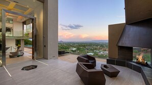 A modern outdoor lounge area with geometric seating, a fire feature, and a view of a cityscape at sunset. - 10,000 sqf Mansion Carved into Camelback - Infinity Pool, Spa, Gym, Rooftop Bar (Phoenix)