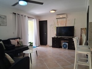 A living room with a black sofa, a small round table, a white chair, a television, and a painting on the wall.