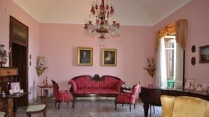A room with a red sofa, two chairs, a chandelier, and a large window with curtains. - ancient 1700 Villa facing Eolie Island (Milazzo)