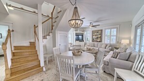 A spacious living room with a high ceiling, a chandelier, a television, and a staircase. - Southside of 30A, Gated beachfront pool sleeps 7 , 2 min walk to Rosemary, NEW ! (seacrest beach)