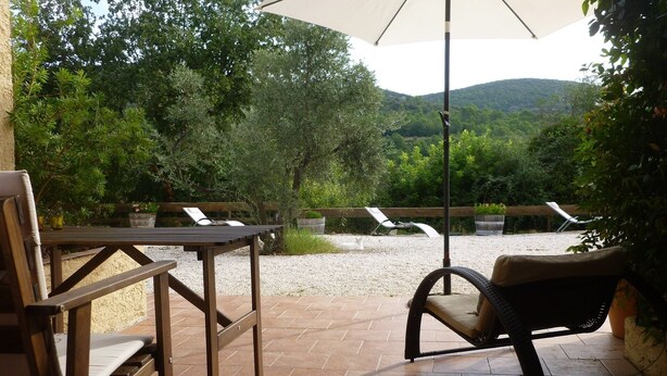 Une terrasse extérieure avec une table et des chaises, un grand parasol et une vue sur une zone boisée.