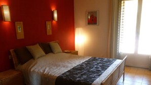 Un lit bien fait, recouvert d’une couvre-lit à motifs, un mur rouge et des lampes fixées au mur.