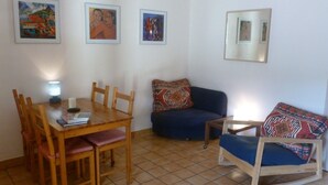 Un coin repas avec une table et des chaises en bois, un canapé bleu et un petit fauteuil. Trois œuvres d’art encadrées ornent le mur.