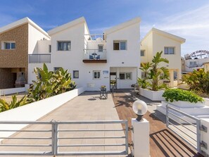 A modern residential building with a flat roof, a balcony with outdoor furniture, and a gated entrance. - A modern 2 bedroom house in the absolute heart of Protaras with fantastic views of the sea (Protaras)
