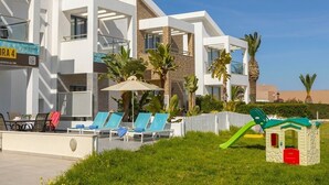 Ein modernes Hotel mit Poolbereich, Sitzgelegenheiten im Freien und einer Kinderspielanlage.
