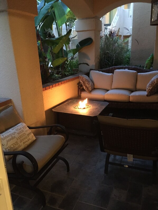 A cozy outdoor seating area with a fire pit, cushioned chairs, and a sofa.