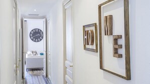 Un pasillo con un reloj grande, un letrero enmarcado que dice 'HOME' y una cama al fondo.