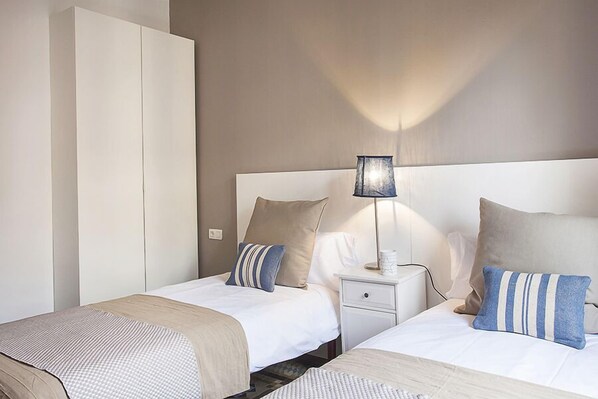 Une chambre d’hôtel avec deux lits, une table de chevet, une lampe et une armoire.