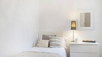Un dormitorio con cama, almohadas, mesita de noche con lámpara y espejo en la pared.
