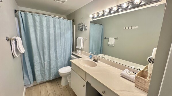 A bathroom with a shower curtain, a toilet, a sink with a mirror, and a towel rack. - Gulf Front Condo---2nd FL --Reserved Parking (Panama City Beach)