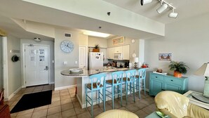 Una cocina con una isla central, taburetes de bar azules, un reloj y un microondas.