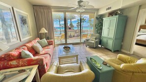 Una sala de estar con un sofá, sillones, una mesita de centro y vistas a una piscina y palmeras.