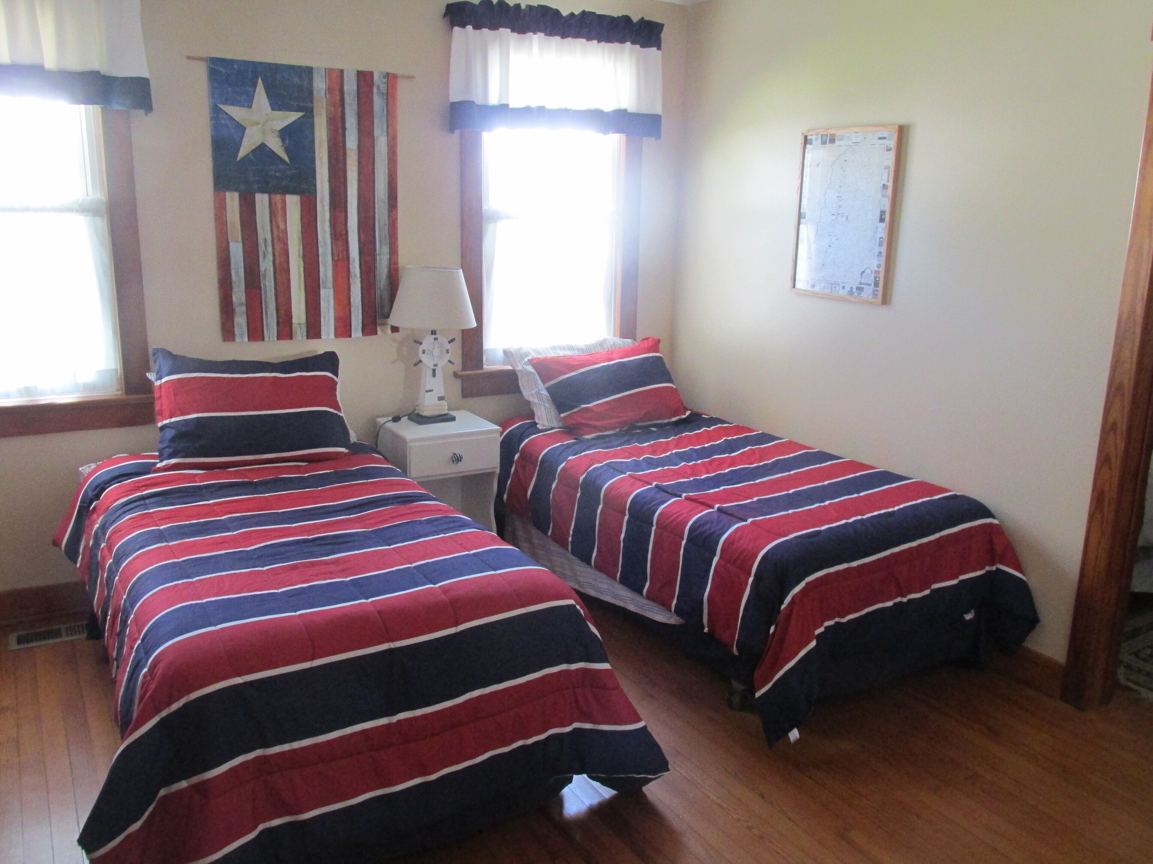 A room with two beds, each with red, white, and blue striped bedding. There is a wall clock and a map on the wall.
