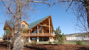 Une grande cabane en rondins avec un toit vert, de nombreux balcons et une vaste terrasse.