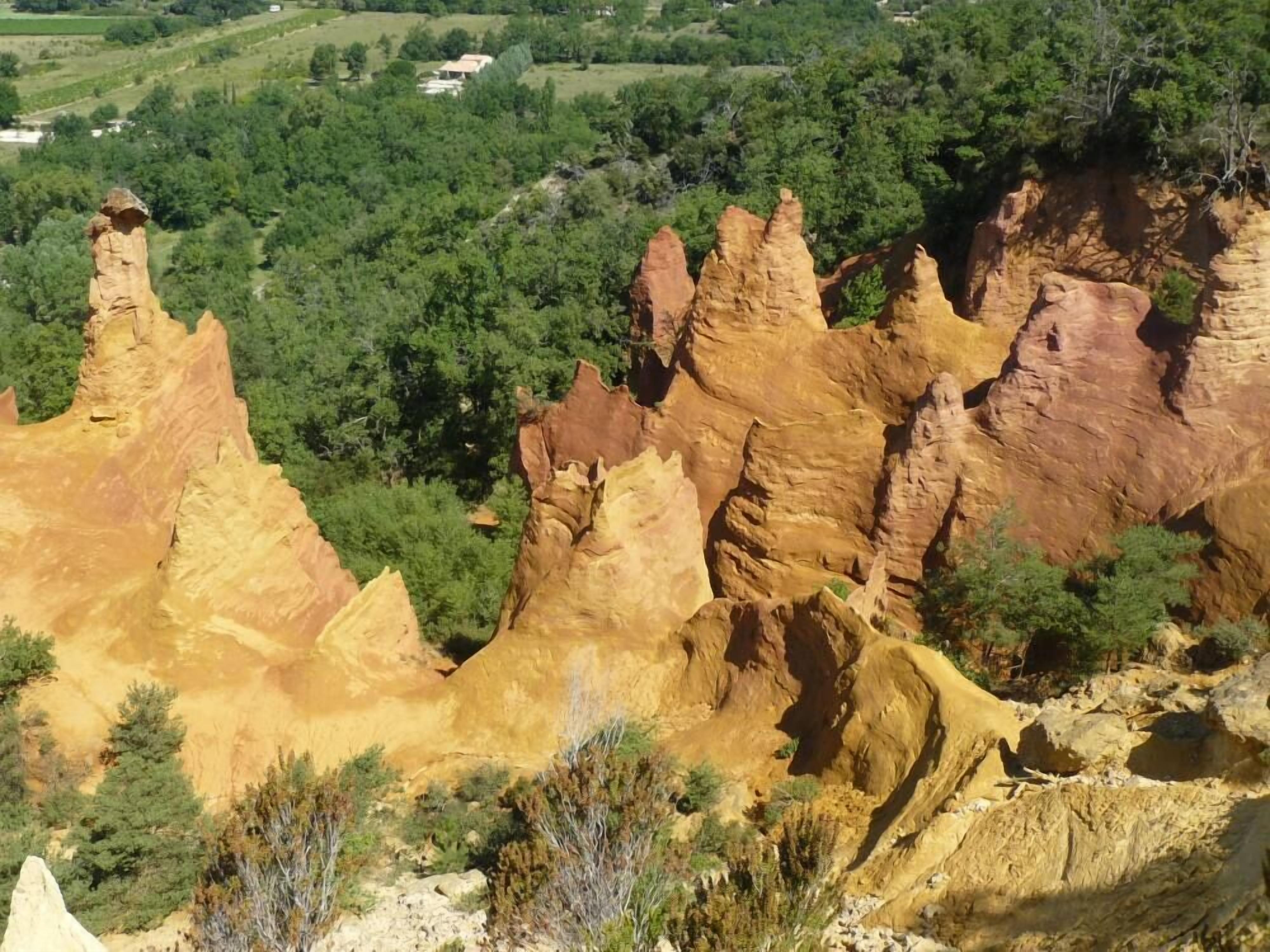 A landscape with prominent rock formations and a distant view of a green valley with buildings.