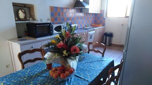 Eine Küche mit Esstisch, der mit einer blauen Tischdecke bedeckt ist, Stühlen, einer Mikrowelle, Schränken und einer Blumenvase.