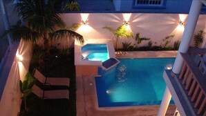 Une piscine avec un jacuzzi, entourée de palmiers et dotée d’une terrasse couverte.
