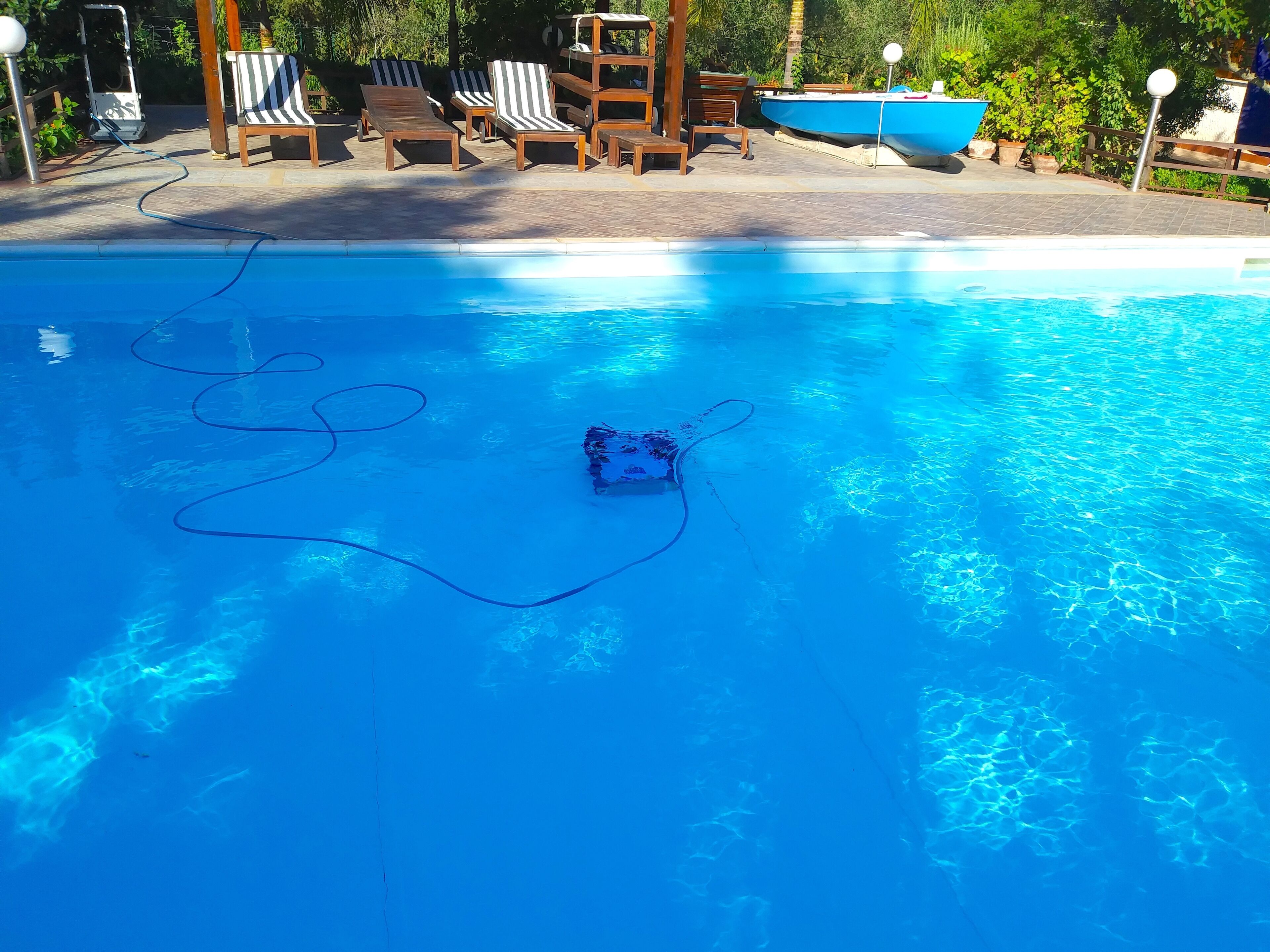 A clear blue swimming pool with lounge chairs and a blue boat.