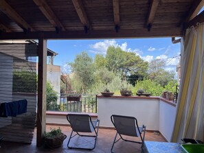 A covered outdoor area with two chairs, a table, and potted plants.