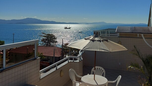 A terrace with a view of the sea, a table with chairs, and a sun umbrella. - Penthouse with Pool, Barbecue and Wonderful Sea View (Florianópolis)