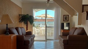 A spacious living area with a sofa set, a wooden cabinet, and a TV. A staircase leads to an outdoor area with a view of a building and a palm tree. - Penthouse with Pool, Barbecue and Wonderful Sea View (Florianópolis)