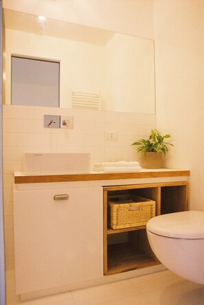 A bathroom with a white sink, a mirror, a toilet, and a plant on the counter.